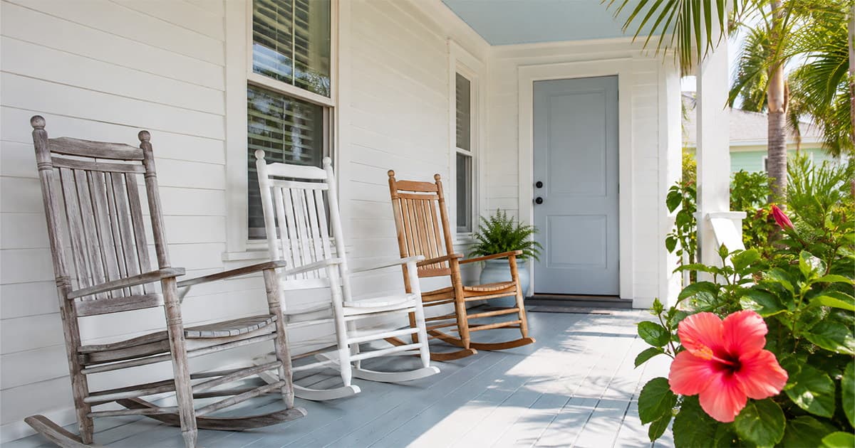 Three empty rocking chairs side by side on the front porch of a single-story Florida home